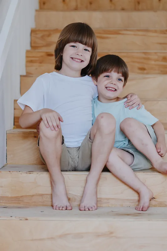 Two smiling boys sitting on wooden stairs, exuding joy and warmth. Their casual outfits and playful expressions create a cheerful atmosphere. Perfect for family themes.