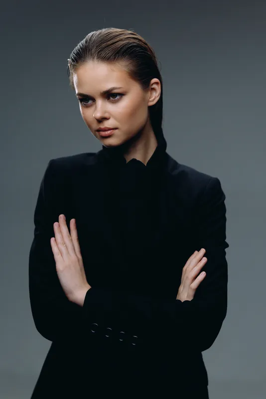 Serious woman in black jacket with crossed arms posing against dark background, showing confidence and focus.