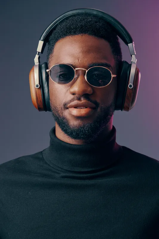 Stylish African man wearing headphones and sunglasses in a black turtleneck, against a colorful gradient background expressing confidence and creativity
