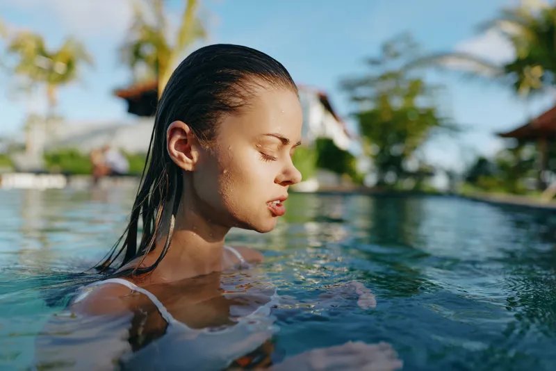 Woman in a pool with wet hair, enjoying a sunny outdoor setting. Close-up captures calm mood and wellness vibe, suited for lifestyle, leisure, and vacation themed projects.