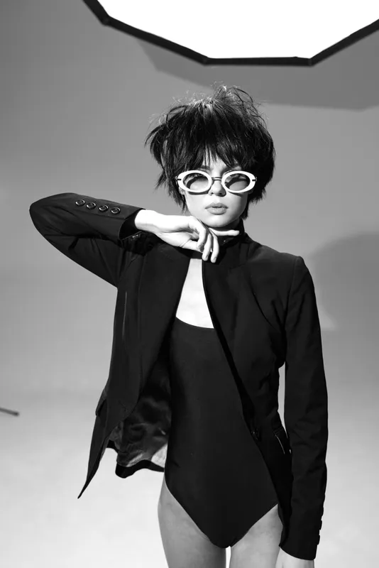 Stylish woman posing in black and white with short hair, sunglasses, and a jacket, showcasing modern fashion and confident attitude.