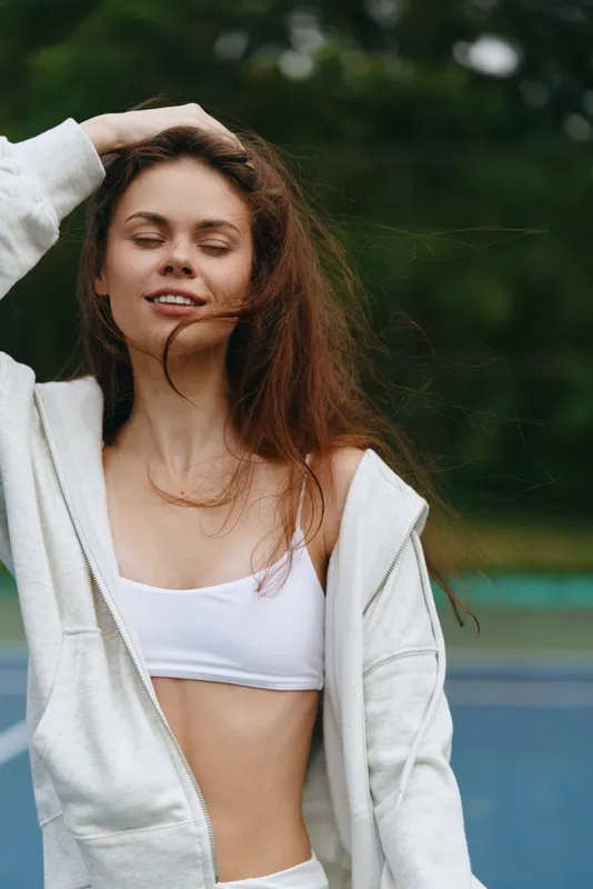 Young woman smiling outdoors in sportswear, promoting healthy lifestyle and fitness, with a green background and casual style for seasonal fitness campaigns