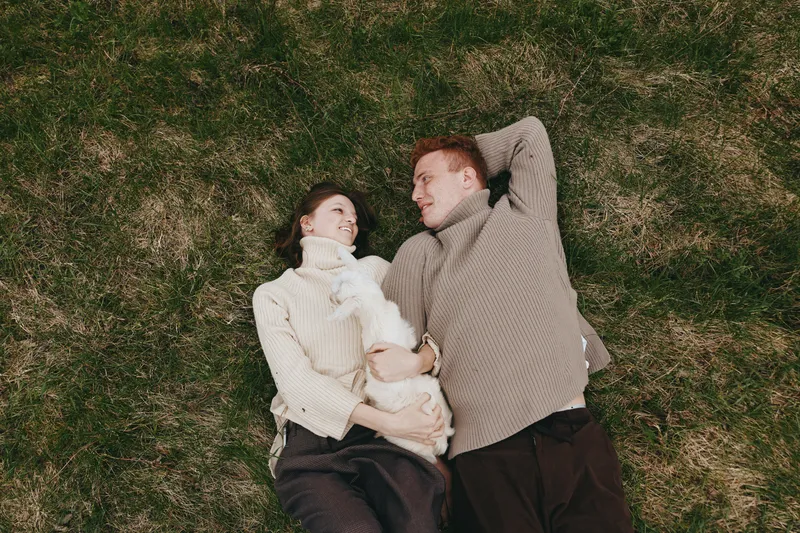 Lifestyle family couple relax on grass outdoors with a baby goat, capturing tender moments on a sunny day, a wholesome scene of affection and calm coexistence in the open countryside