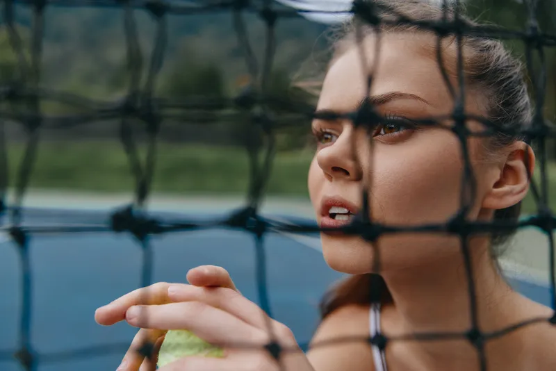 Young woman focused on tennis practice, wearing sports attire and displaying determination, with a blurred court background and natural lighting