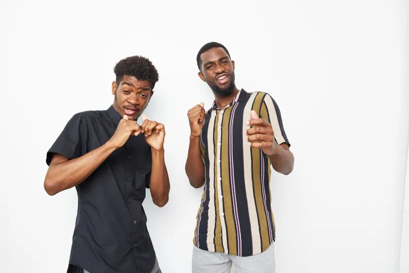 Two joyful black men playfully dancing together, wearing stylish casual clothes in a bright studio. Their energy and smiles radiate a vibrant atmosphere.
