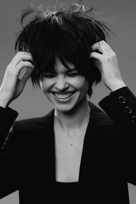 Smiling woman enjoying moment in black and white artistic portrait with messy hair and dark jacket