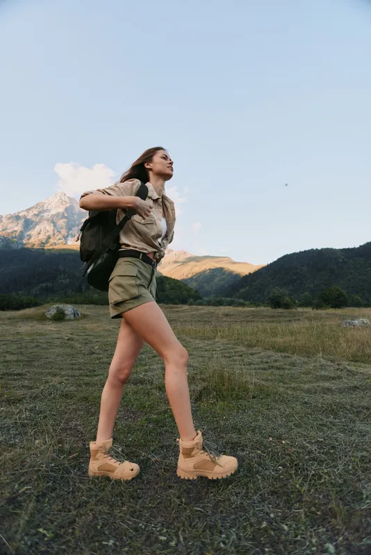 Woman hiking outdoors with a backpack, exploring a mountain landscape on a sunny day, casual attire, energetic pose, natural colors, expansive scenery