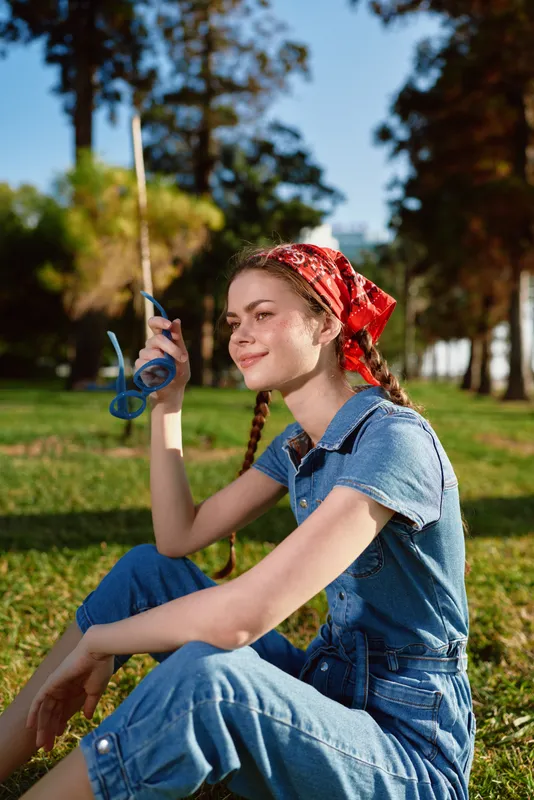 lifestyle woman in modern boho-western denim street style sitting outdoors with a red bandana and fishing rod, natural film color, relaxed and sunny mood