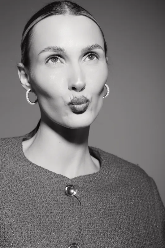 Portrait of a fair skinned white woman with slicked back hair making a kiss face in black and white studio.