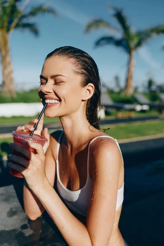 Woman enjoys a smoothie by the poolside on a sunny summer day, lifestyle moment of casual relaxation, pool, palm trees, refreshing beverage, joyful vibe