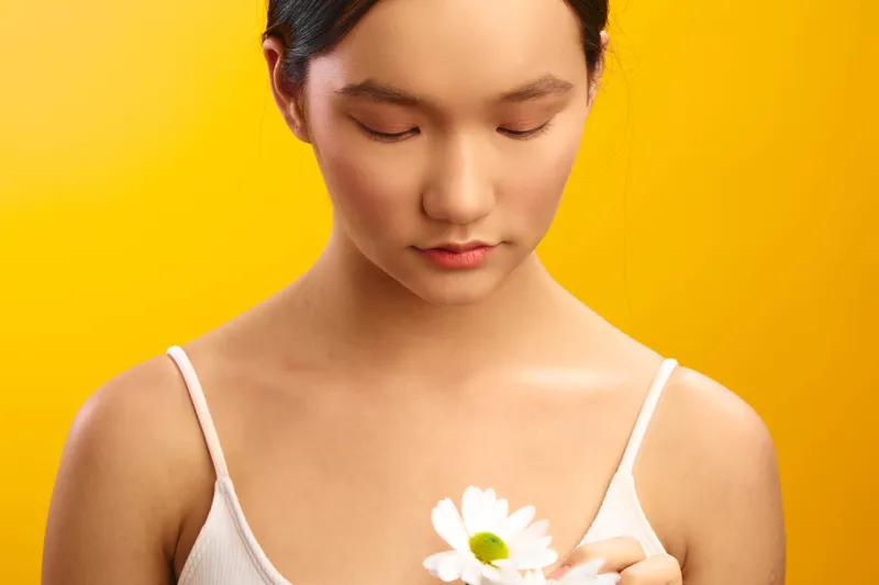 asian woman with a soft gaze holds a delicate white flower against a warm yellow backdrop, creating a calm, graceful portrait with serene and contemplative mood.