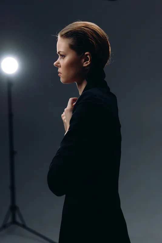 Profile of a serious woman in black jacket with studio light and dark background