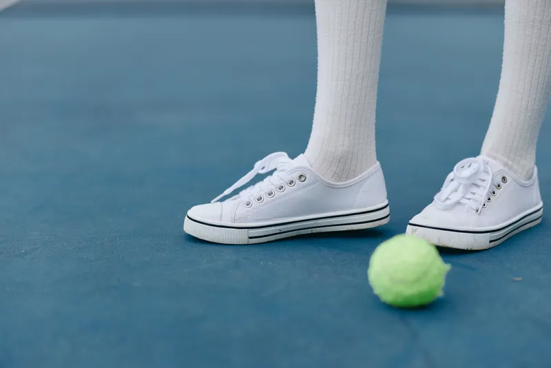 Young athlete in white sport shoes on blue tennis court with green tennis ball, showcasing passion for sports and training in a vibrant setting