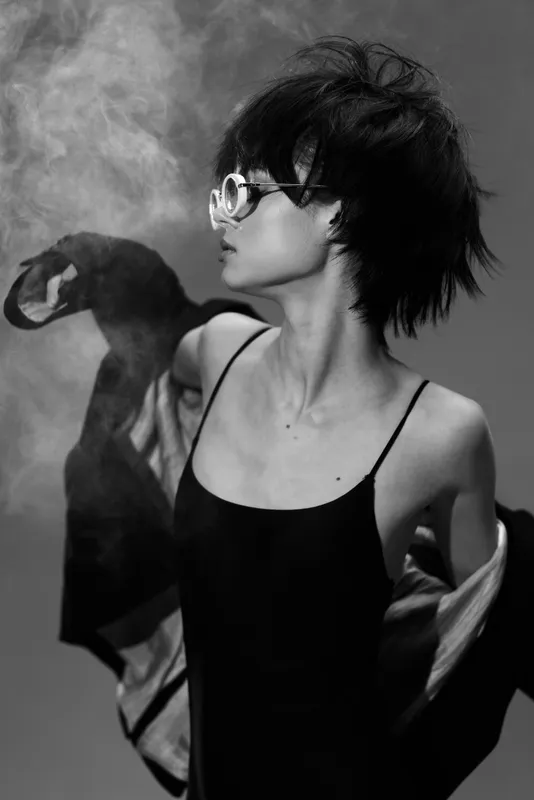 Black and white portrait of a young woman with short hair wearing sunglasses and a sleeveless dress, expressing freedom and style.