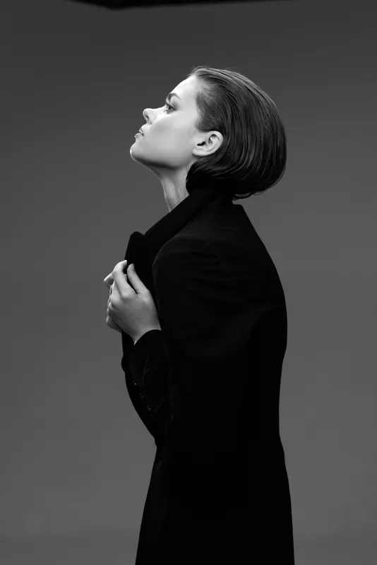 Black and white profile of a thoughtful woman in elegant clothing with hands near chest and serene expression.