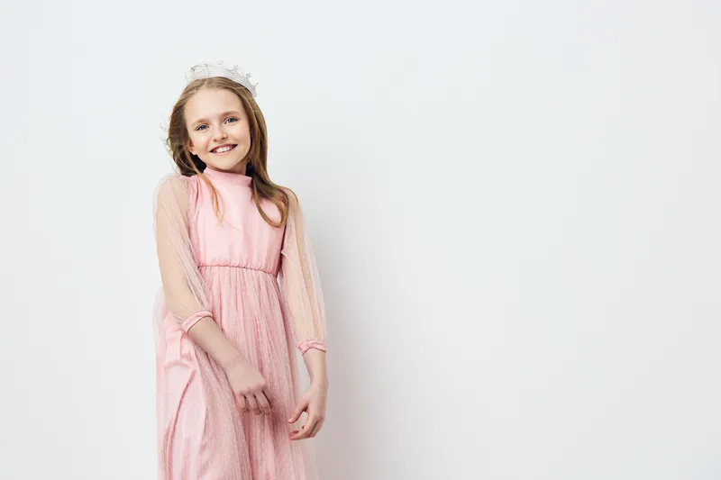 A young girl in a pink dress smiles joyfully against a light background, showcasing innocence and happiness in a seasonal portrait