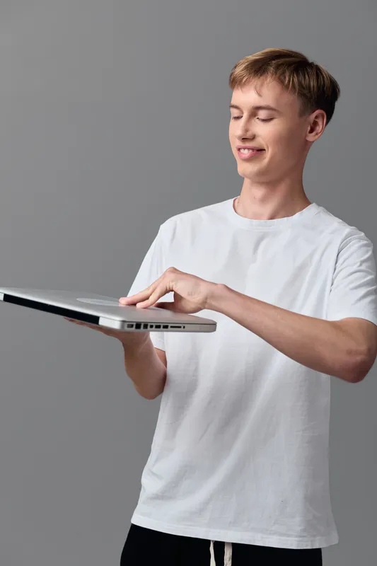 Hands holding laptop and tablet for youth learning and everyday technology, modern casual setup with grey background, screen activity and focused workflow for education and remote work