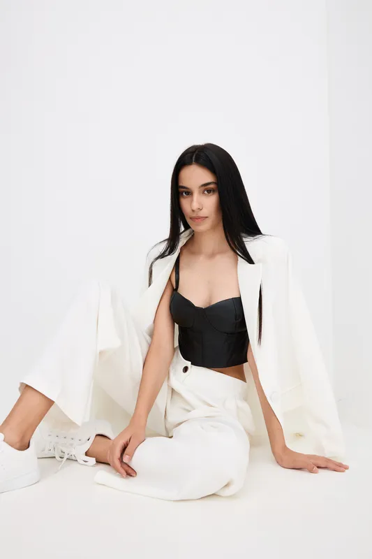 stylish woman sitting in white pants and jacket with black top, long dark hair, minimalist background, modern fashion, youthful and poised elegance