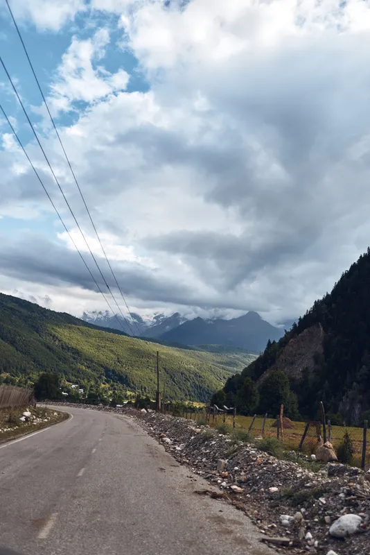 Road through a mountain landscape under dramatic clouds with a valley in the distance, offering a tranquil scenic outdoor journey