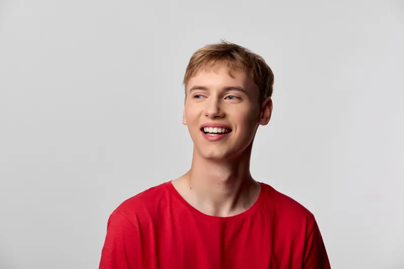 Young man with smile in a red shirt, casual lifestyle imagery for happiness and approachability, friendly expression, daylight studio setup, upbeat mood and energizing vibe