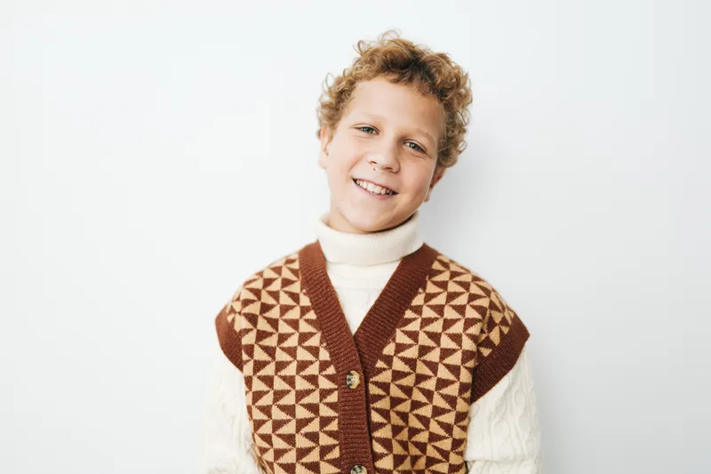An authentic portrait of a cheerful student in a geometric knit vest, capturing school life and a subtle game theme with warm light and a natural smile.