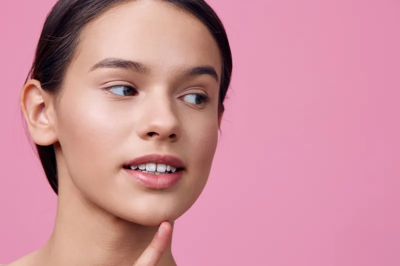 Portrait of a young woman with braces, expressing confidence and beauty against a soft pink background, perfect for beauty and dental care concepts