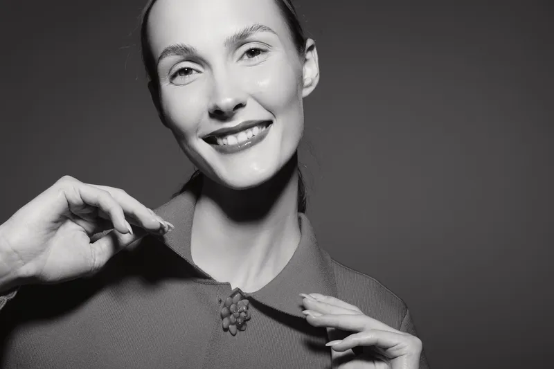 Smiling Caucasian woman with light skin wearing vintage textured coat and decorative brooch in black and white portrait. Elegant style concept.