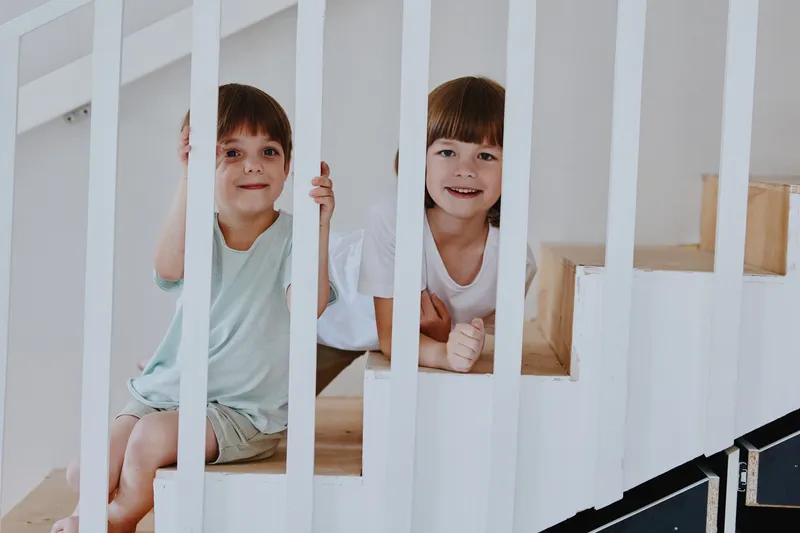 Happy children sitting on the stairs, expressing joy and playfulness in a bright and modern interior. Their smiles add warmth to the scene, creating a cheerful atmosphere.