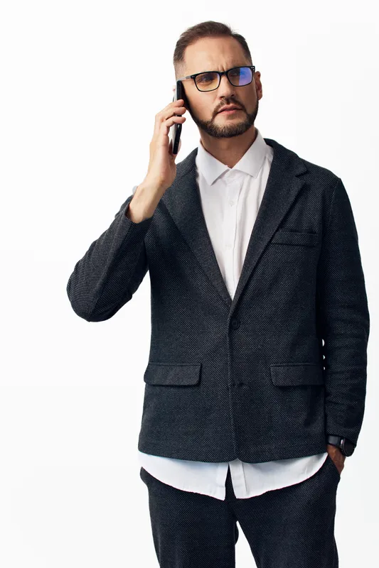 A business professional man stands against an isolated white background, projecting confidence and calm as he speaks on a mobile phone during a moment of focus.