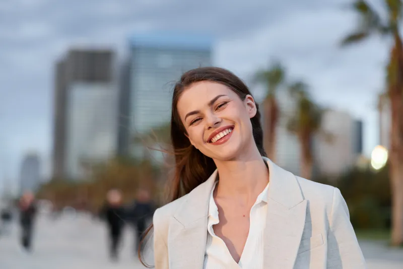 Confident businesswoman smiling outdoors in modern urban setting, showcasing professional attire and positive emotions, perfect for empowering business visuals.