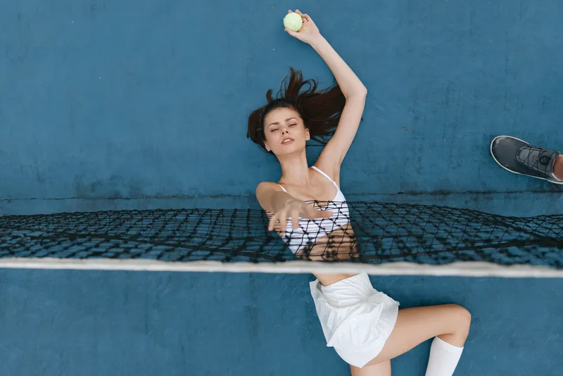 Young woman playing tennis, holding a tennis ball, demonstrating athleticism and grace on a blue court with a net, showcasing a sporty and active lifestyle