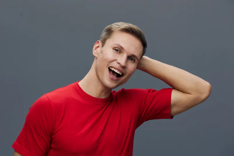 smiling young caucasian man red t-shirt casual look camera hand behind head gray background cheerful positive emotion happy lifestyle concept digital detox
