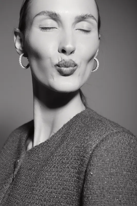 Young white woman with light skin and closed eyes makes a kissing face, wearing earrings and textured jacket. Concept of emotions, beauty, and fashion portrait.