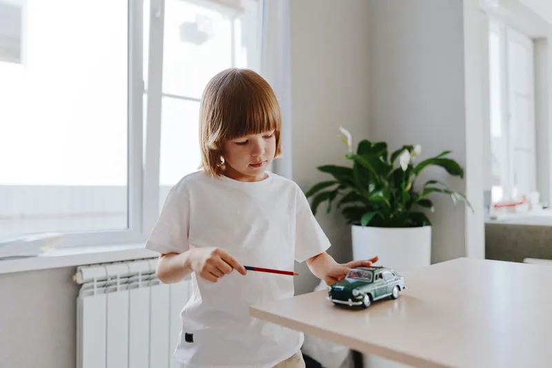 A young boy playing with a toy car, focused and engrossed in his activities, showcasing creativity and joy during playtime in a bright, modern room.