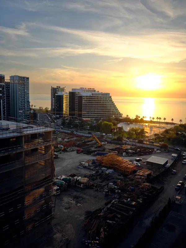 Sunset construction city ocean skyline palm trees with coastal high-rise buildings and cranes overlooking waterfront development, golden light reflecting on sea and urban beach
