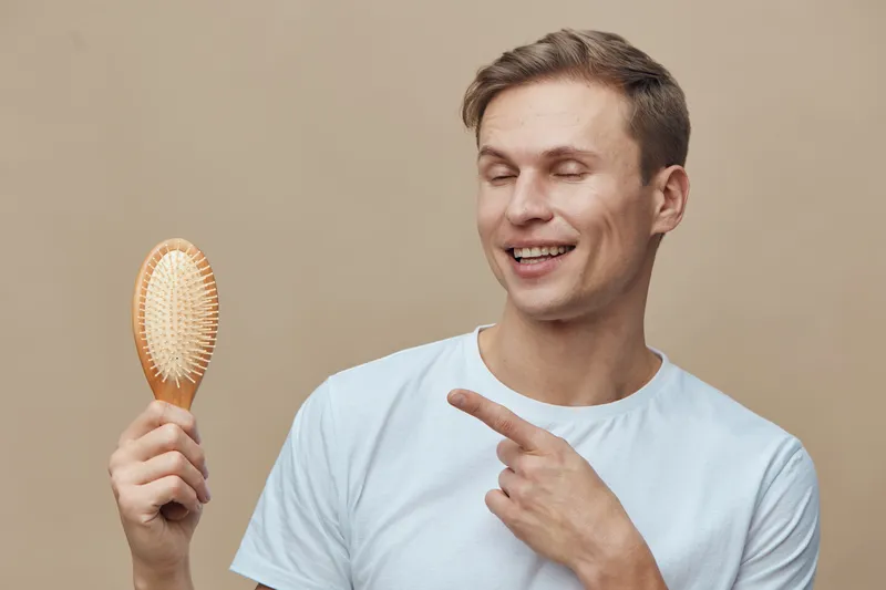 smiling young caucasian man wear white t-shirt hold wooden hairbrush point finger closed eyes beige background digital detox concept