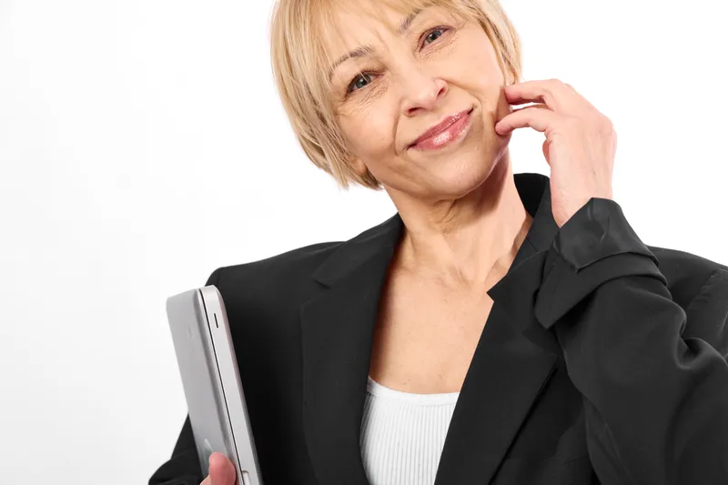 Senior businesswoman portrait with smartphone, woman smiles, hand at cheek, thoughtful expression, white background, office attire, communication and technology use, calm confidence