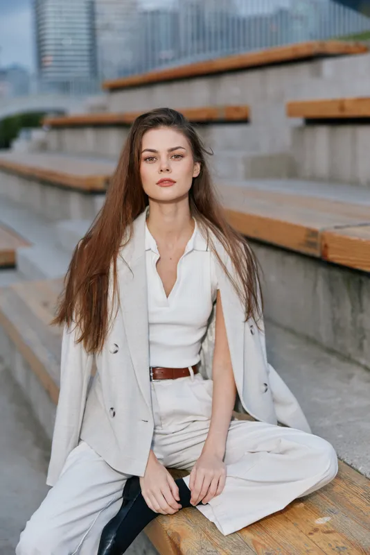 Confident businesswoman sitting outdoors in stylish attire, portraying professionalism and elegance amid a modern urban backdrop.