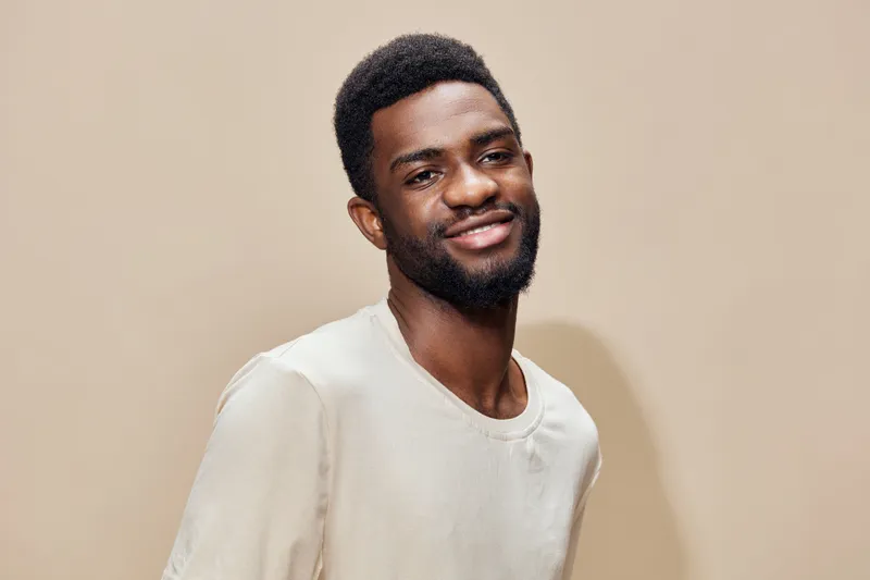 Smiling young African man in casual beige shirt against a light neutral background, showcasing confidence and happiness in a modern portrait