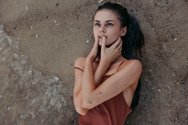 thoughtful woman with dark hair in red dress standing against rough textured wall, expressing deep emotion and introspection