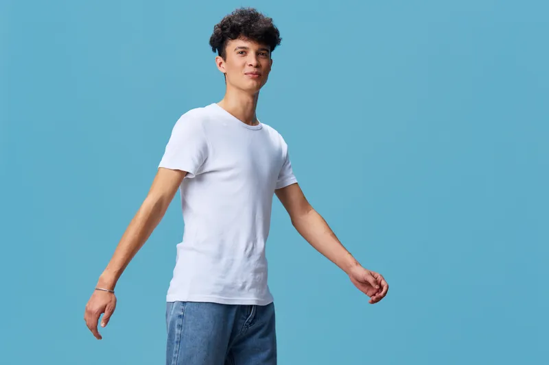 young man in white t-shirt and jeans posing against blue background with casual confident expression and relaxed posture in studio setting