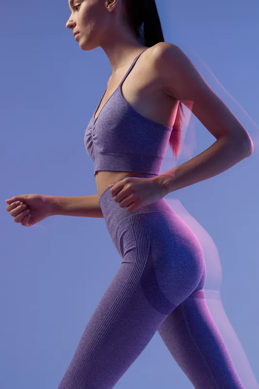 Active woman sport fitness running in seamless purple workout outfit with focused expression, illustrating energy, strength, and healthy lifestyle in dynamic motion.