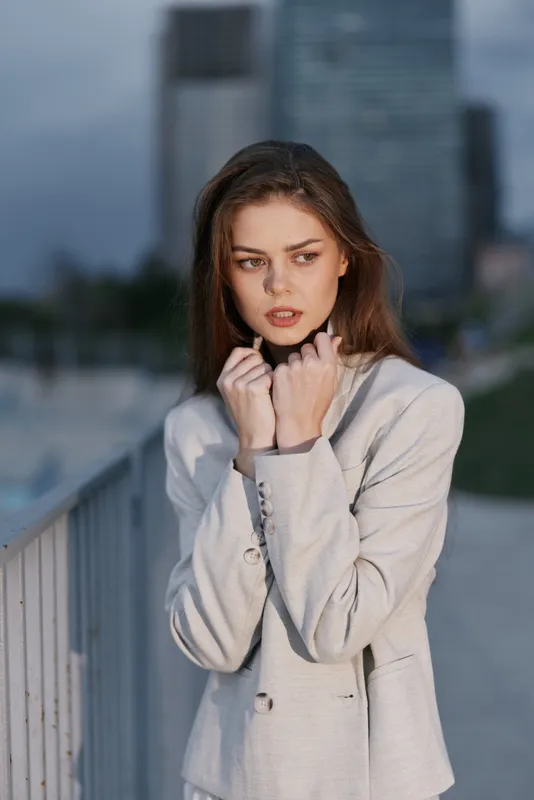 Young woman with anxious expression in light gray business suit standing outdoors against blurred urban background showing psychological stress and worry