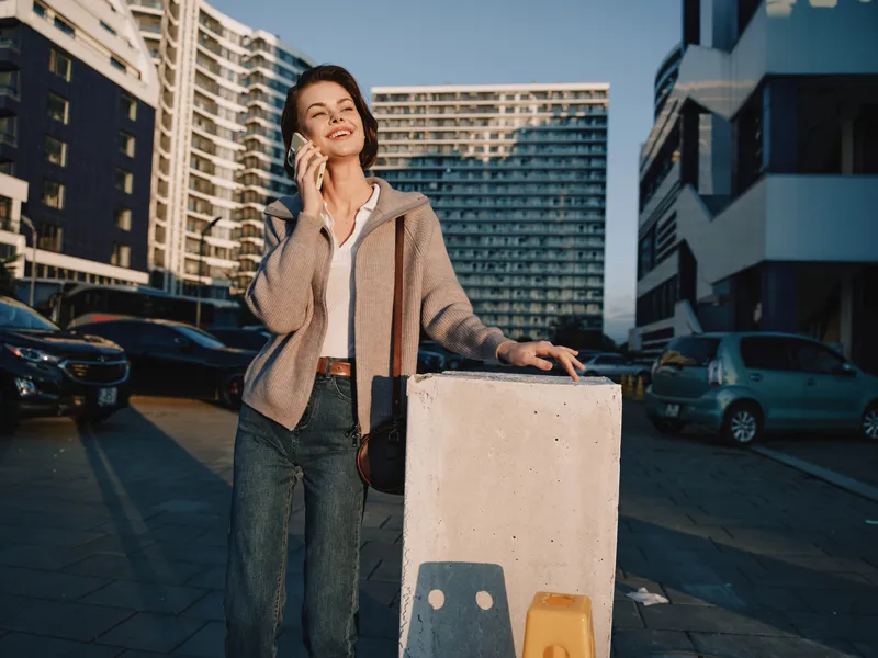 An upbeat urban professional speaks on a smartphone in a modern street scene. She wears a casual jacket and jeans, smiles warmly, and exudes confidence in a positive city atmosphere.