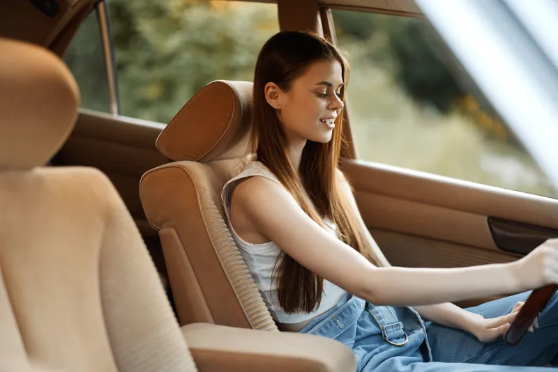 Young woman enjoying a drive in a vintage car, exuding happiness and relaxation in a soft, warm color palette. Perfect for lifestyle and travel themes.