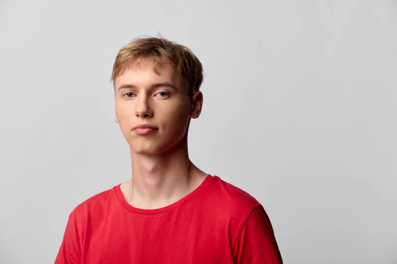 Young man in a red shirt stands against a neutral studio background, relaxed pose and soft lighting, simple fashion style for lifestyle, everyday vibe with clean composition and calm mood