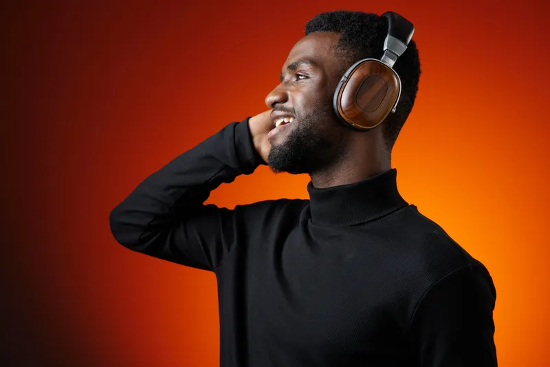 Young African man enjoying music with headphones, smiling confidently against an orange background, showcasing his stylish black turtleneck in a vibrant setting