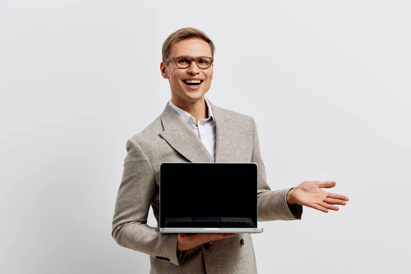 smiling man presenting laptop hold in hand wear glasses gray suit concept digital nomad work remote cheerful expression on white background