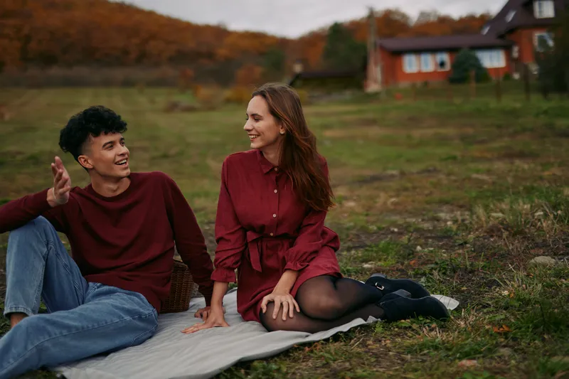 Candid portrait of a young couple sharing a genuine conversation while sitting on a blanket in a rustic meadow, captured with natural light and authentic, relaxed expressions conveying real