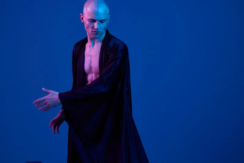 A striking image of a man in a flowing black robe, expressing dynamic movement against a vibrant blue backdrop. The scene evokes a sense of grace and artistic flair.